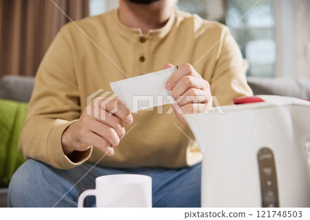 Close of male hands holding with sachet with negative space to insert your text and teacup and electric kettle nearby in desk. 121748503