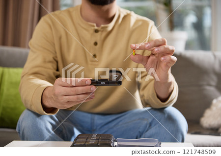 Cropped photo of male hand holding open pillbox in one hands and pill, vitamin or diet supplement in another. Immunity and routine. 121748509