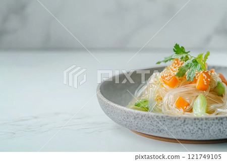 Delicate glass noodles with fresh vegetables and sesame served elegantly on a neutral plate with soft lighting 121749105