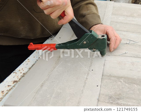 riveting device in operation in male hands, side view, stapling thin metal sheets using a riveter 121749155