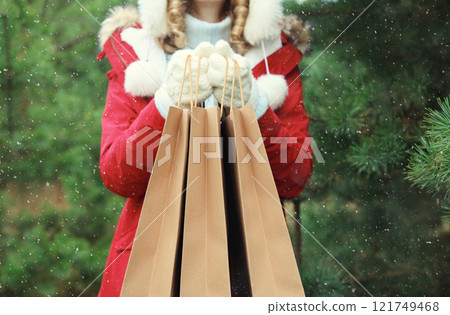 Purchase, holidays, female hand holding showing paper shopping bags, gift against Christmas tree 121749468