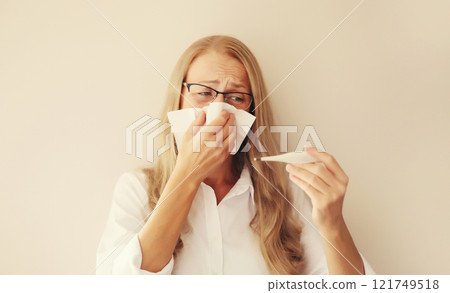 Sick woman sneezing blow nose with tissue, measuring checking body temperature looks at thermometer Sick woman sneezing blow nose with tissue, measuring checking body temperature looks at thermometer 121749518