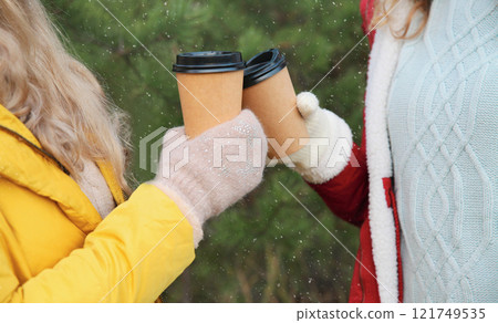 Close up two women friends, female hands holding cups of coffee drink, Christmas trees in winter Close up two women friends, female hands holding cups of coffee drink, Christmas trees in winter 121749535