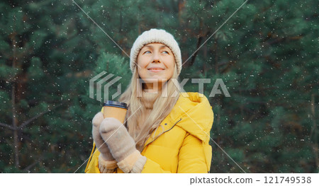 Winter day, happy smiling woman holding cup of coffee drink enjoys snow, against Christmas tree 121749538