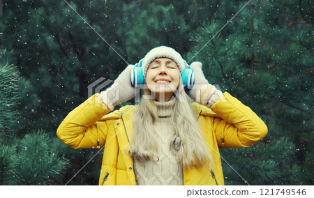 Happy young woman enjoy listening to music with headphones in winter forest against Christmas tree Happy young woman enjoy listening to music with headphones in winter forest against Christmas tree 121749546