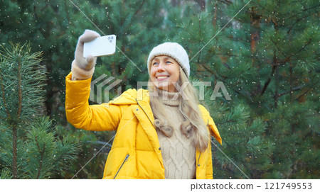 Happy smiling woman taking selfie with smartphone in winter park against Christmas tree, using phone Happy smiling woman taking selfie with smartphone in winter park against Christmas tree, using phone 121749553