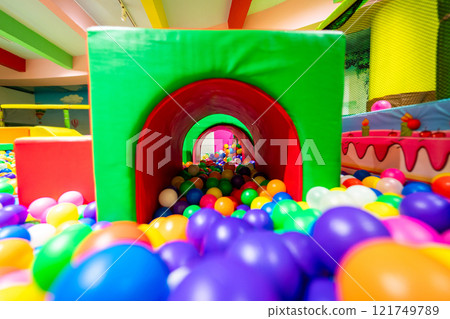 A colorful play tunnel leading into a vibrant ball pit in an indoor playground. 121749789