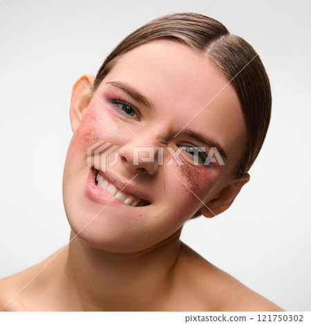Portrait of young, beautiful woman, grimacing with gold glitter accentuating vibrant makeup against white studio background. Concept of modern beauty. Portrait of young, beautiful woman, grimacing with gold glitter accentuating vibrant makeup against white studio background. Concept of modern beauty. 121750302
