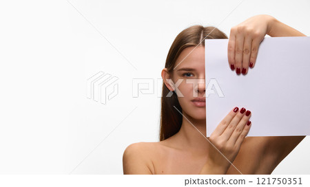 Close-up of a woman holding blank sheet against white studio background, with a strong gaze, emphasizing elegance and symmetry. Concept of natural beauty. 121750351