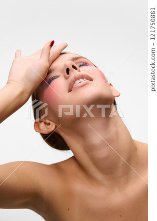 Young woman, with bright make up, tilting head back and put hand on face, against white studio background. Concept of unique beauty. 121750881