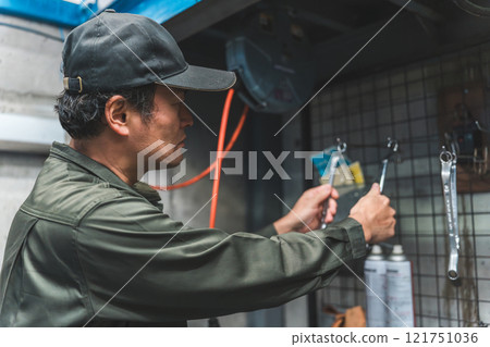 A male auto mechanic tidying up wall-mounted tools 121751036