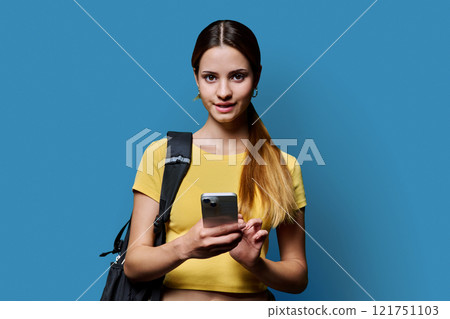 Young beautiful girl student with backpack using smartphone on blue studio background Young beautiful girl student with backpack using smartphone on blue studio background 121751103