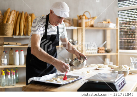 Elderly man baker greases pieces of dough Elderly man baker greases pieces of dough 121751845