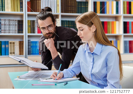Teenage student girl studying with male teacher inside classroom library 121752777