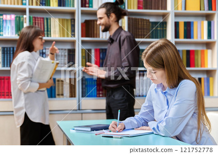 Teenage girl college student studying, teachers talking in background, library interior Teenage girl college student studying, teachers talking in background, library interior 121752778
