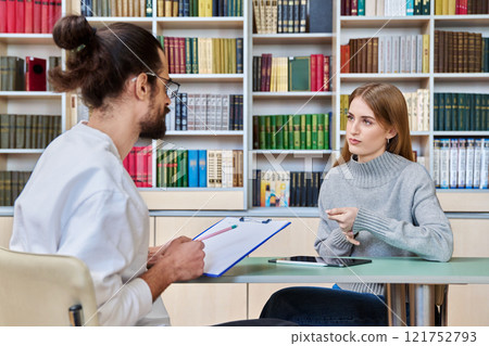 Teenage student girl talking with male teacher, social worker, school counselor in library 121752793