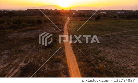 Country road through pasture. Sunrise over a dirt road. Dusty rural road landscape and a beautiful sunset sky use for natural background. 121754087