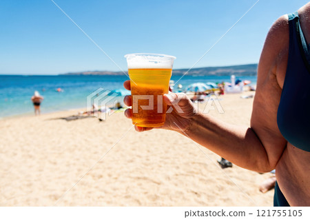 A woman is holding a plastic cup of beer on a beach. A woman is holding a plastic cup of beer on a beach. 121755105
