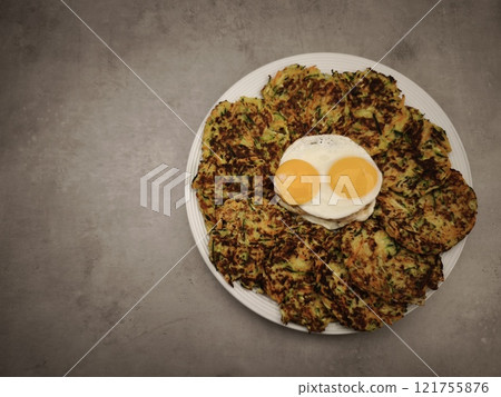 Zucchini and carrot pancakes with fried eggs on a white plate 121755876