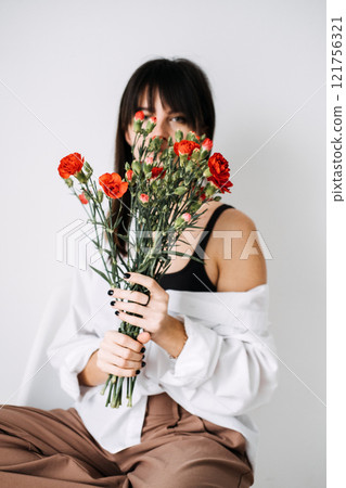 Woman holding red carnations, hiding face behind flowers. Visual storytelling, minimalist composition, natural beauty, floral aesthetic, Instagram-ready content. Woman holding red carnations, hiding face behind flowers. Visual storytelling, minimalist composition, natural beauty, floral aesthetic, Instagram-ready content. 121756321