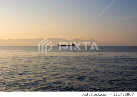 a cargo barge ferry floats at dawn on the sea against the backdrop of mountains in the fog, cargo and passenger transportation 121756907