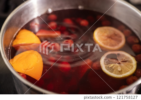 A pot of homemade fruit compote with orange slices, lemon slices, and berries simmering in water. 121758127