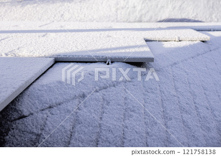 Snow-covered solar panels on a rooftop, showcasing a serene winter morning with frost and light shadows. 121758138