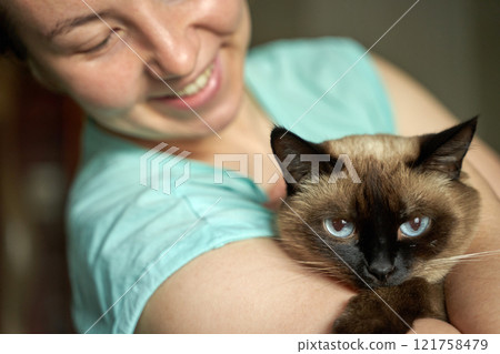Caucasian female adult smiling while holding siamese cat with blue eyes 121758479