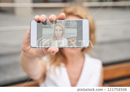 Caucasian female adult taking self-portrait with smartphone, blurred background 121758506