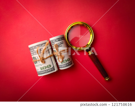 Top view banknotes and vintage magnifying glass on a red background. 121758616
