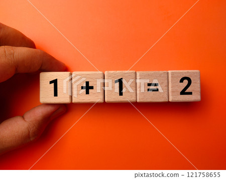 Hand holding wooden block with number 1 plus 1 equal to 2 on orange background. Education concept. Hand holding wooden block with number 1 plus 1 equal to 2 on orange background. Education concept. 121758655