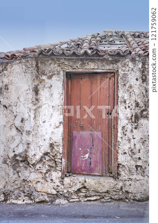 Old abandoned house or home with a weathered stone wall and red wooden door. Vintage and aged residential building built in a traditional architectural style or design with a blue sky background Old abandoned house or home with a weathered stone wall and red wooden door. Vintage and aged residential building built in a traditional architectural style or design with a blue sky background 121759062