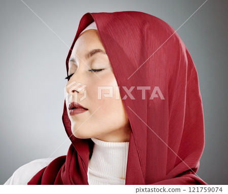 Stylish young muslim woman in a red hijab with her eyes closed on a grey studio background. Middle eastern woman wearing makeup and a headscarf while feeling calm and showing the beauty in modesty Stylish young muslim woman in a red hijab with her eyes closed on a grey studio background. Middle eastern woman wearing makeup and a headscarf while feeling calm and showing the beauty in modesty 121759074