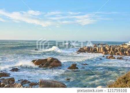 Copyspace at sea with a cloudy blue sky background and rocky coast in Western Cape South Africa. Ocean waves crashing onto boulders at a beach. Peaceful scenic landscape for a relaxing summer holiday 121759108