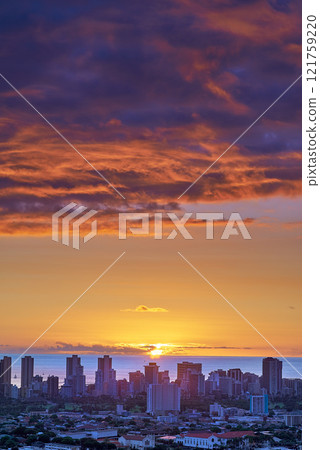 A sunset over a city skyline near the sea with cloudy purple and orange sky. Sunrise over a blue horizon near urban landscape with copy space. Peaceful holiday destination at night in Waikiki, Hawaii 121759220