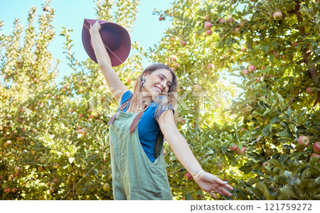 Excited young woman jumping for joy in an apple orchard on a sunny day outside. Happy and cheerful farmer feeling optimistic, free and full of energy after a fruitful harvest on her successful farm 121759272
