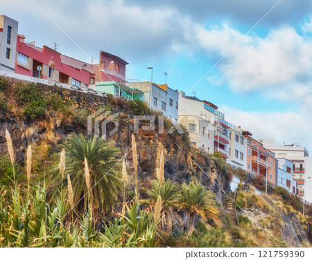 City view of residential houses or buildings on a hill cliff in Santa Cruz, La Palma, Spain. Historical spanish, colonial architecture and palm trees in tropical village of famous tourism destination City view of residential houses or buildings on a hill cliff in Santa Cruz, La Palma, Spain. Historical spanish, colonial architecture and palm trees in tropical village of famous tourism destination 121759390