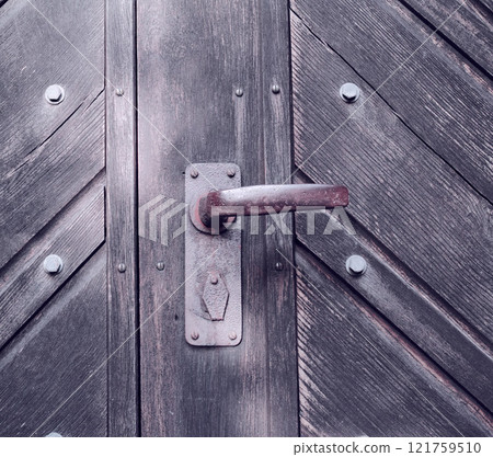 A strange old wooden entrance door with a rusted door handle. A vintage door knob. Closeup of a traditional door with a handle and a lock. A copy space background. The gate knob is made of metal. 121759510