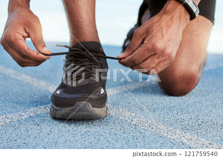 Active athletic man preparing for a practice run to increase stamina for a competitive race on an Olympic track. Closeup of a fit african american athlete tying his shoelaces before running outside. 121759540