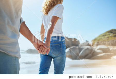 Closeup of a loving mature couple holding hands while walking on the beach in summer. Affectionate husband and wife enjoying stroll by the sea while on holiday. Man and woman on a relaxing date 121759597