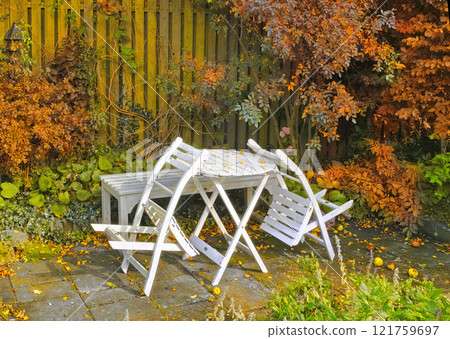 White wooden chairs and table in a serene, peaceful, lush, private backyard at home in autumn. Patio furniture set in outdoor space, seating in an empty and tranquil garden with scrub plants White wooden chairs and table in a serene, peaceful, lush, private backyard at home in autumn. Patio furniture set in outdoor space, seating in an empty and tranquil garden with scrub plants 121759697
