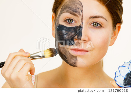 Female applying black mud mask to face 121760918