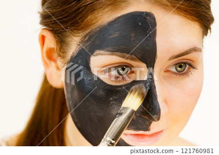 Female applying black mud facial mask 121760981