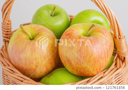 Two different varieties of apples in a wicker basket on a gray background. Fruits, apples. Two different varieties of apples in a wicker basket on a gray background. Fruits, apples. 121761856