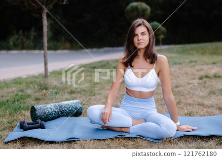 Young woman relaxing on yoga mat after outdoor workout in park Young woman relaxing on yoga mat after outdoor workout in park 121762180
