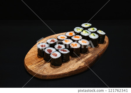 Creative minimalist display of assorted Maki sushi rolls on a wooden platter against a dark backdrop, emphasizing vibrant colors and exquisite Japanese culinary art with a modern aesthetic. Creative minimalist display of assorted Maki sushi rolls on a wooden platter against a dark backdrop, emphasizing vibrant colors and exquisite Japanese culinary art with a modern aesthetic. 121762341