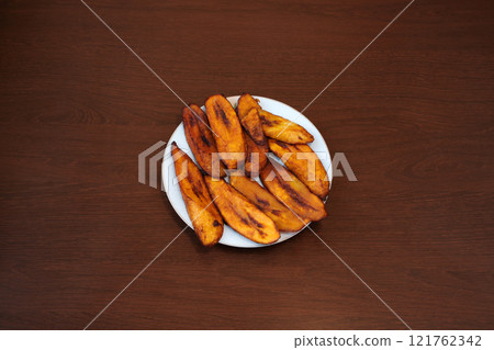 Fried plantain bananas on wooden background. Traditional African recipe cuisine Fried plantain bananas on wooden background. Traditional African recipe cuisine 121762342