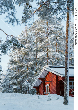 Red wooden cabin in snowy Finnish forest. Concept of winter, nature, and peaceful seasonal retreat in Finland 121762458