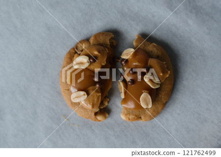 Close up of homemade american traditional chocolate chip cookie with peanut butter, caramel and peanuts topping. Cookie broken in half. 121762499