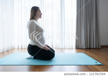 Gen Z pregnant woman sitting on yoga mat at home. Workout, yoga and fitness at home, pregnancy concept. Pre-natal. 121762504